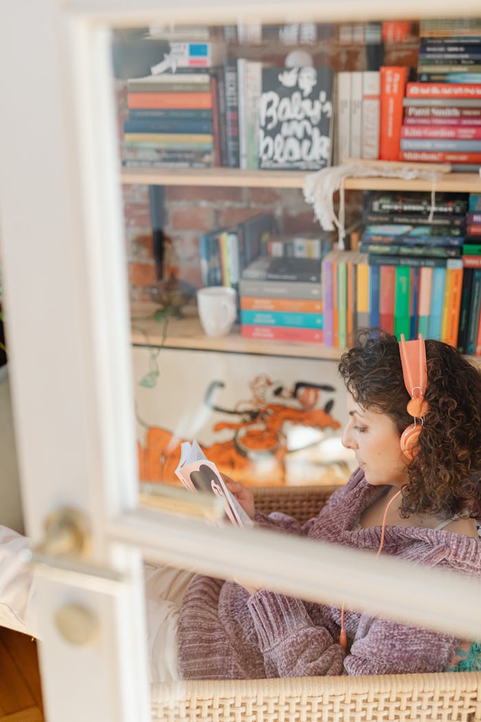 our-journey-01 Woman relaxing indoors with book and headphones, near a bookshelf.